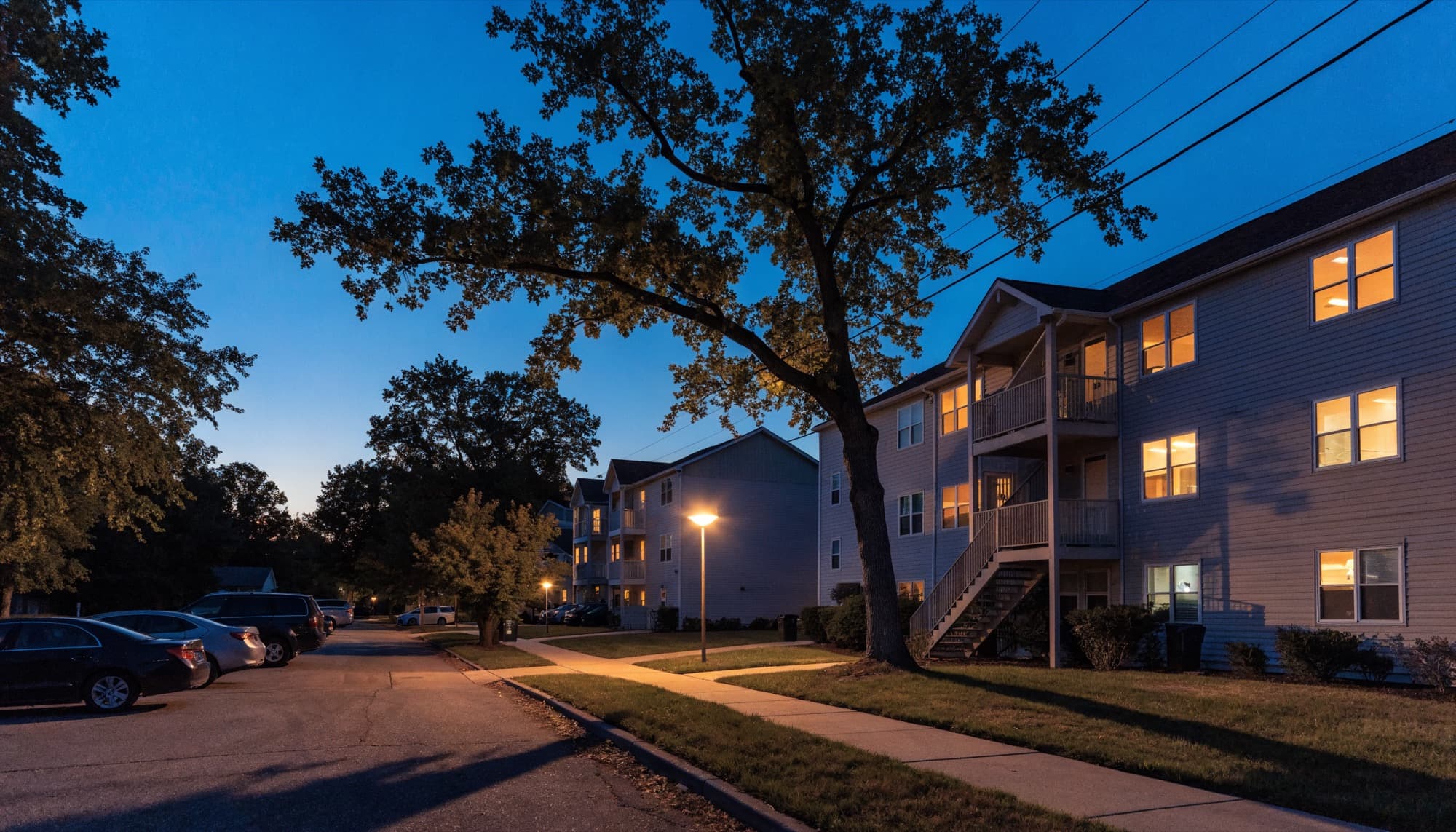 An apartment community at dusk, street lights on and windows lit.